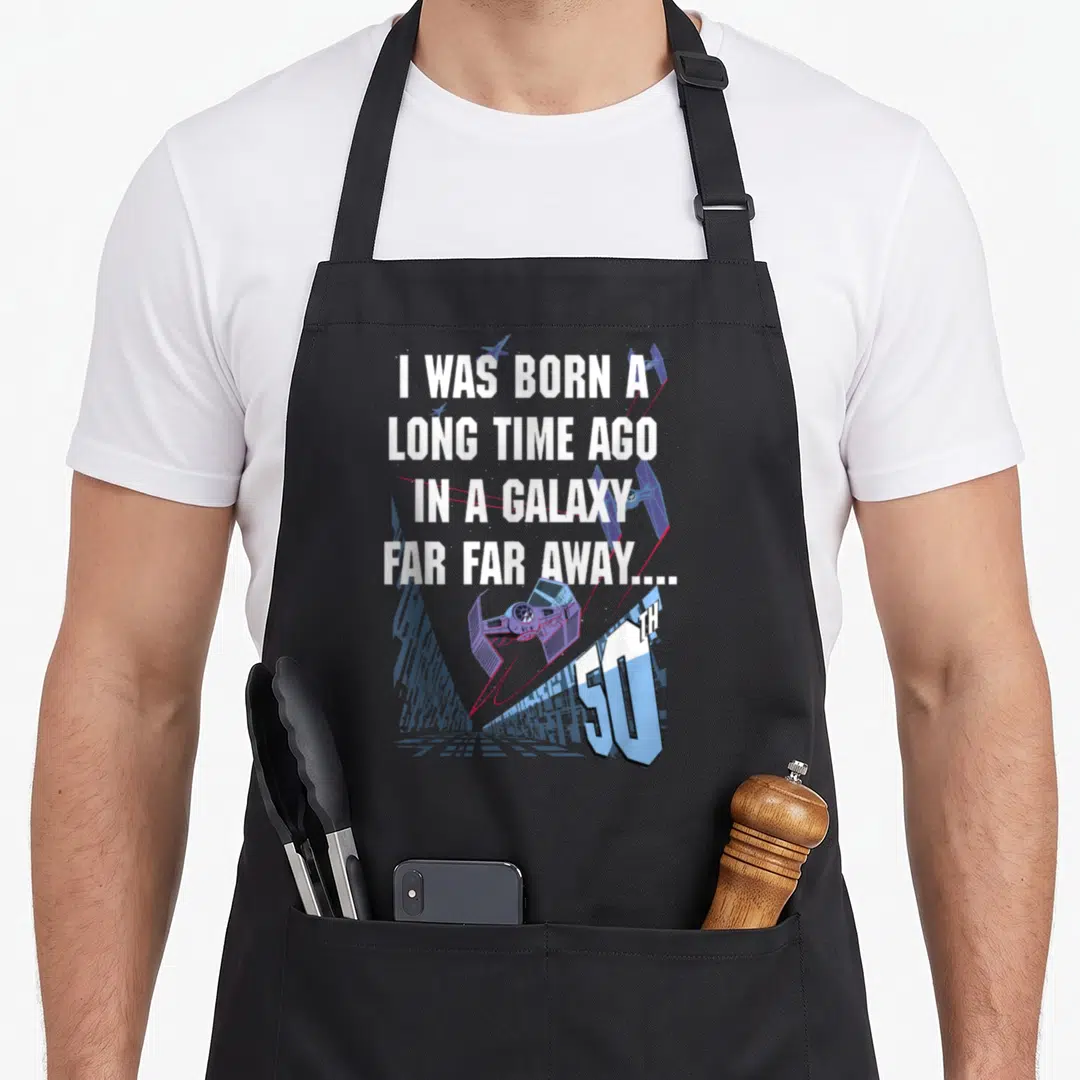 Ago birthday apron - Purple TIE fighter and blue cityscape with 50th birthday quote — shown on a black cotton canvas apron against a white background