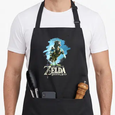 Wild legend apron - Link riding a rearing horse above Zelda text with integrated sword in blue and brown — shown on a black cotton canvas apron against a white background