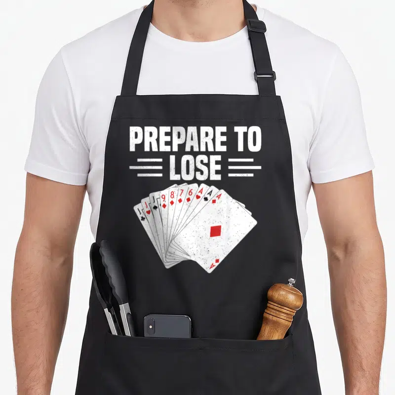 Score game aprons - PREPARE TO LOSE text above spread playing cards distressed print — shown on a black cotton canvas apron against a white background