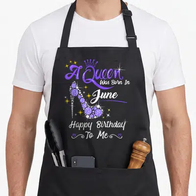 June heel birthday apron - Purple high heel shoe with A Queen was Born In June text and crown — shown on a black cotton canvas apron against a white background