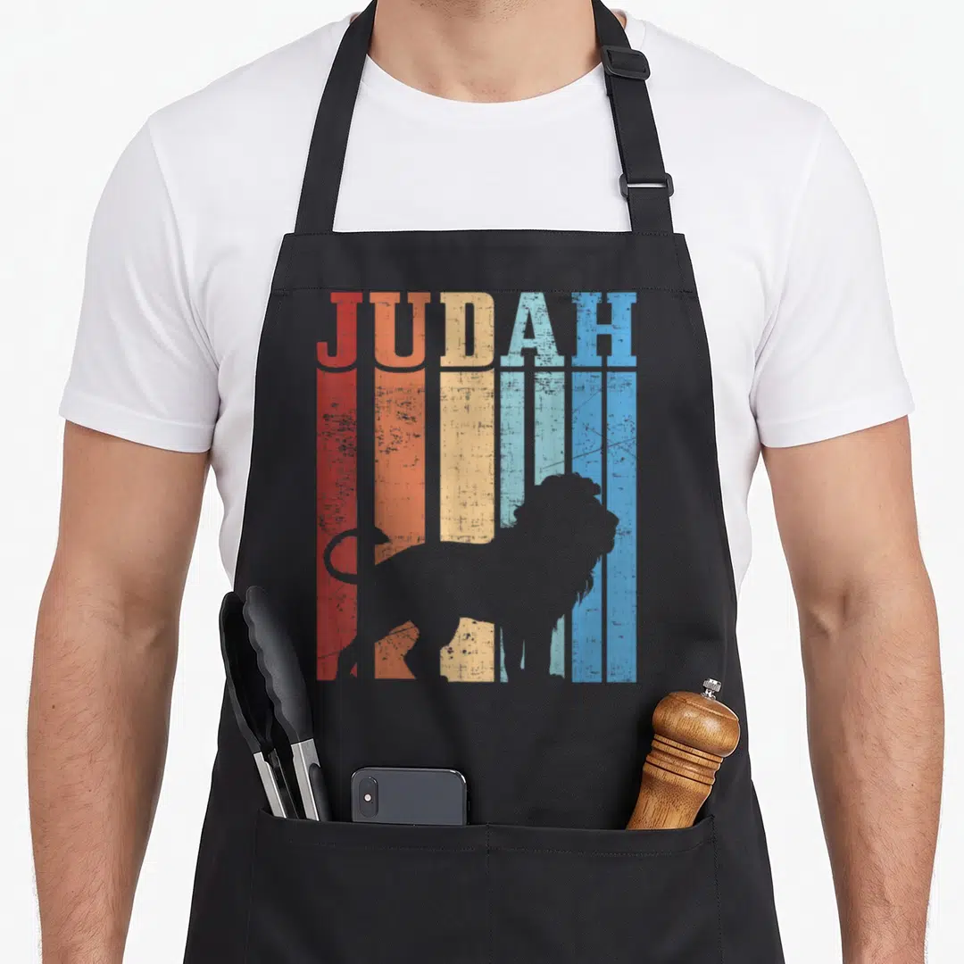 Judah hebrew lions apron - Grey lion silhouette over five vertical stripes in red orange yellow and blue with JUDAH text — shown on a black cotton canvas apron against a white background