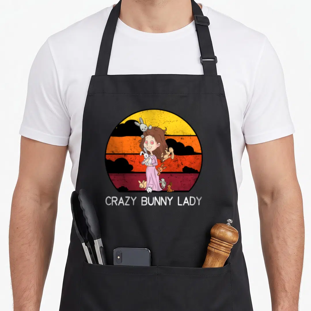 Cute bunny rabbit apron - Cartoon woman holding rabbits inside yellow orange red circle with black clouds and white — shown on a black cotton canvas apron against a white background