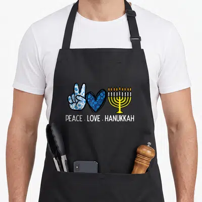 Peace hanukkah apron - Peace sign hand, heart, and menorah symbols with text PEACE LOVE HANUKKAH — shown on a black cotton canvas apron against a white background
