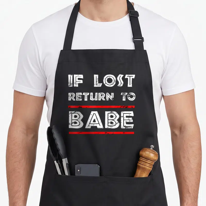 Return couple apron - White distressed text IF LOST RETURN TO BABE with red horizontal lines — shown on a black cotton canvas apron against a white background