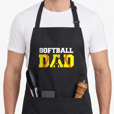 Softball field dad apron - SOFTBALL DAD text with yellow letters containing red stitching and grey batter silhouette — shown on a black cotton canvas apron against a white background