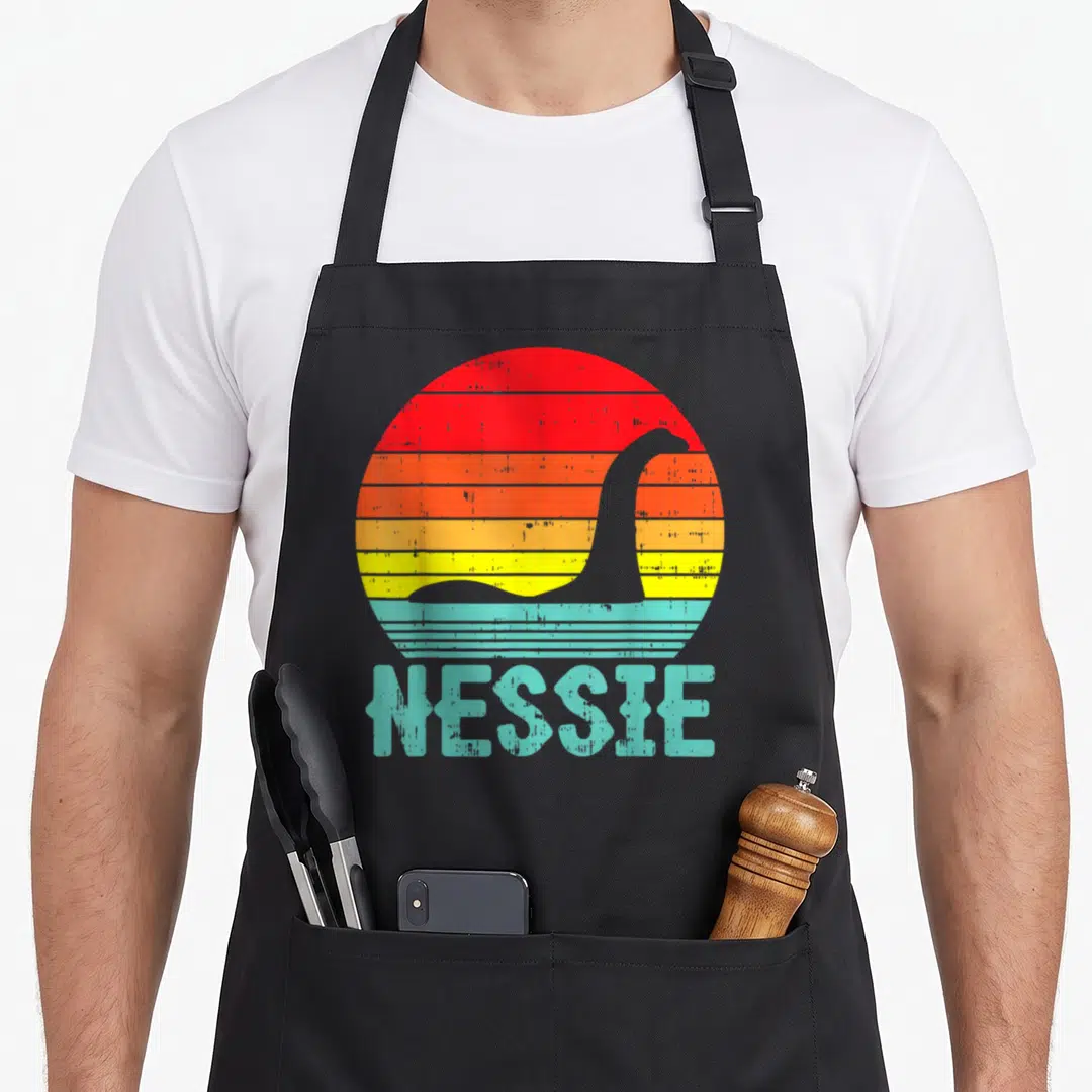 Nessie animal apron - Retro Nessie silhouette in striped red orange yellow teal sun with text — shown on a black cotton canvas apron against a white background