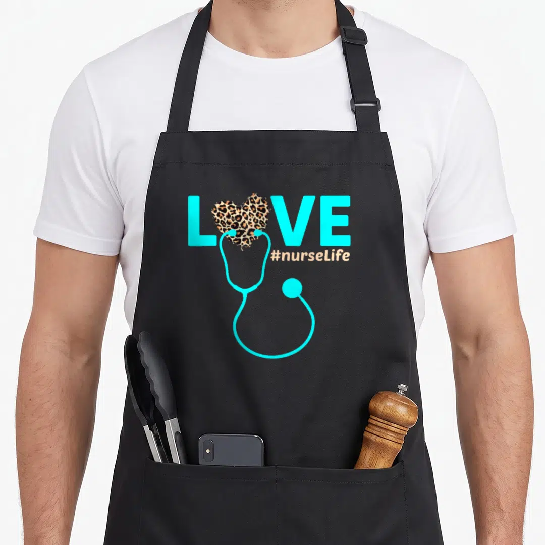 Lpn nurse apron - Cyan stethoscope and leopard heart replacing O in LOVE with #nurseLife hashtag — shown on a black cotton canvas apron against a white background