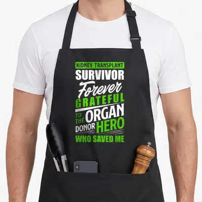 Receiver organ apron - Green and white stacked text reading Kidney Transplant Survivor and Organ Donor Hero — shown on a black cotton canvas apron against a white background