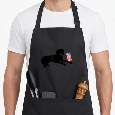 Lab 4th of july apron - Black silhouette of a leaping dog holding a small waving USA flag in its mouth — shown on a black cotton canvas apron against a white background