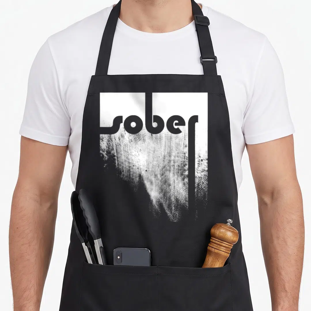 Sober sobriety apron - Distressed grey and white typography reading sober on a black background — shown on a black cotton canvas apron against a white background