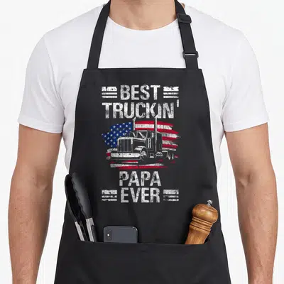 Flag semi truck apron - Best Truckin Papa Ever text with semi-truck and distressed USA flag graphic — shown on a black cotton canvas apron against a white background