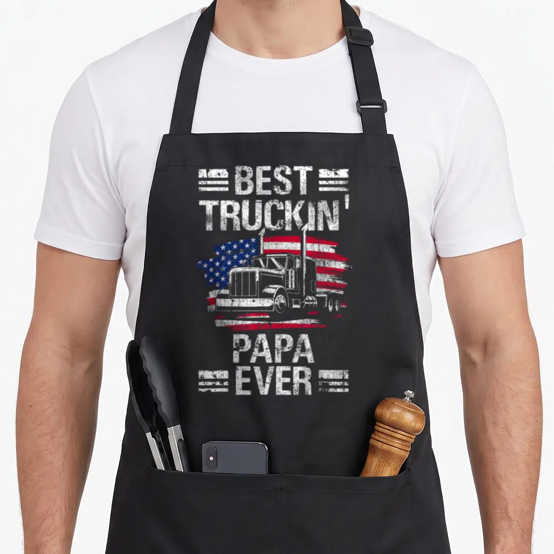 Flag semi truck apron - Best Truckin Papa Ever text with semi-truck and distressed USA flag graphic — shown on a black cotton canvas apron against a white background