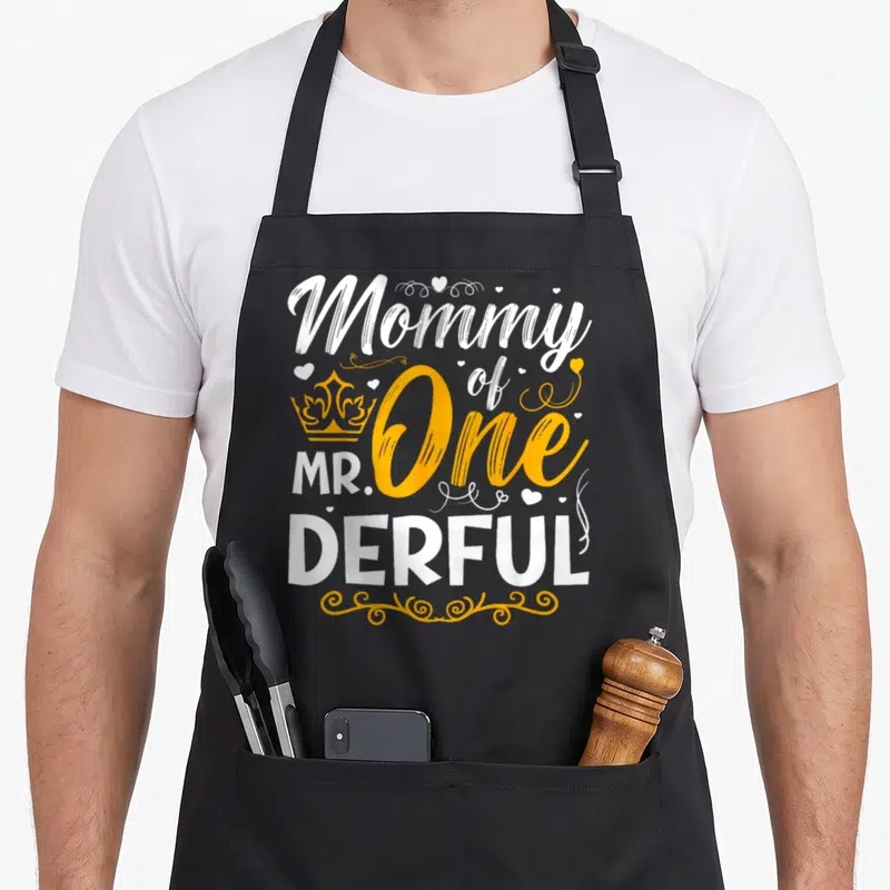 Derful family aprons - Stacked white and yellow text reading Mommy of Mr One Derful with crown and hearts — shown on a black cotton canvas apron against a white background