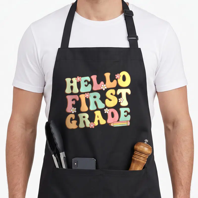 Hello grade cute teacher aprons - Hello First Grade pastel text with flowers and pencil illustration — shown on a black cotton canvas apron against a white background