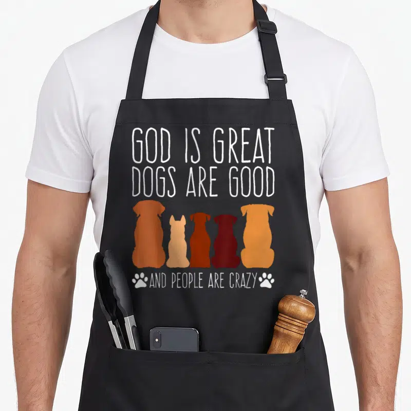 Cheeky dog apron - Five dog silhouettes in orange and brown below white text reading God Is Great Dogs Are Good — shown on a black cotton canvas apron against a white background