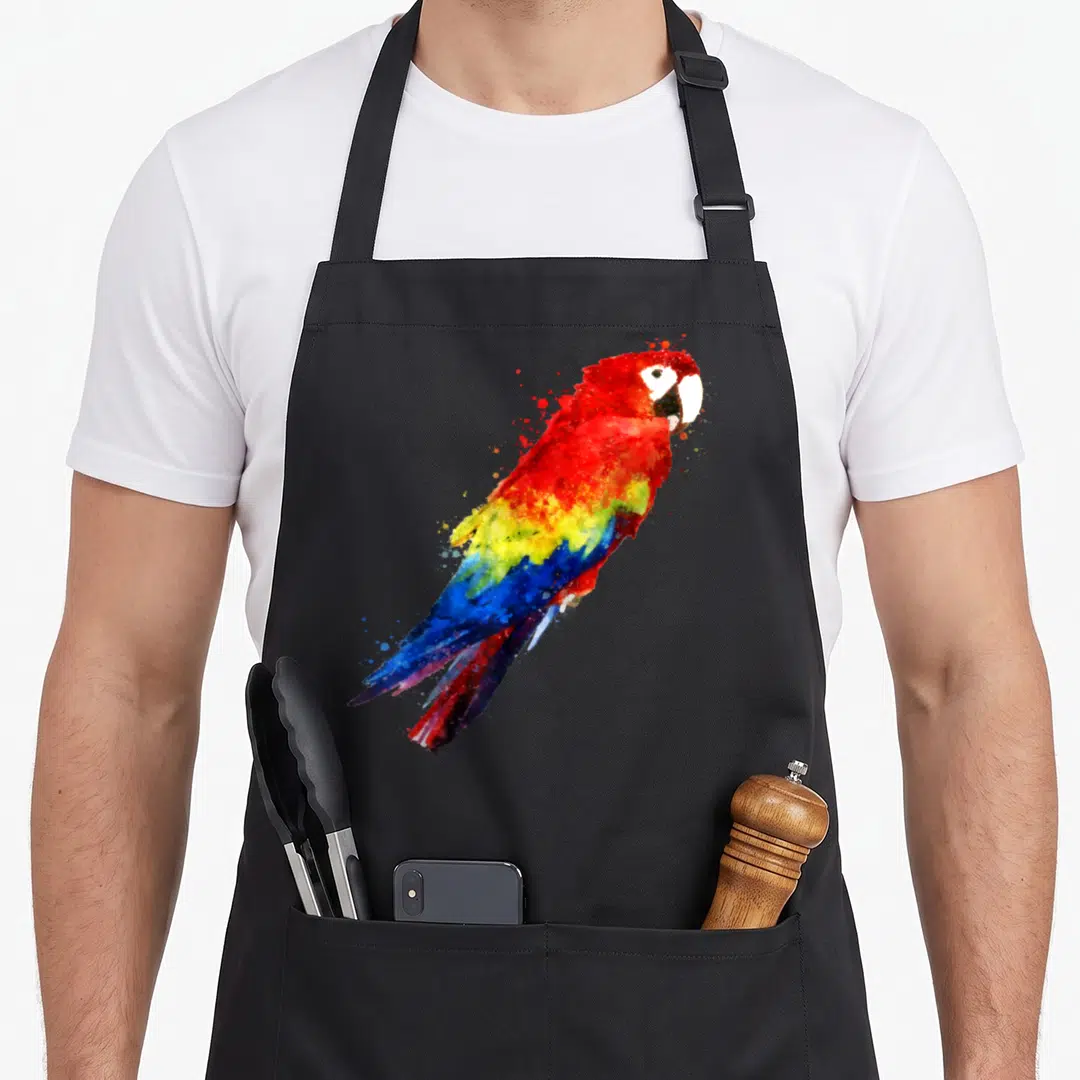 Watercolour bird apron - Centered watercolor macaw with red yellow and blue paint splashes — shown on a black cotton canvas apron against a white background