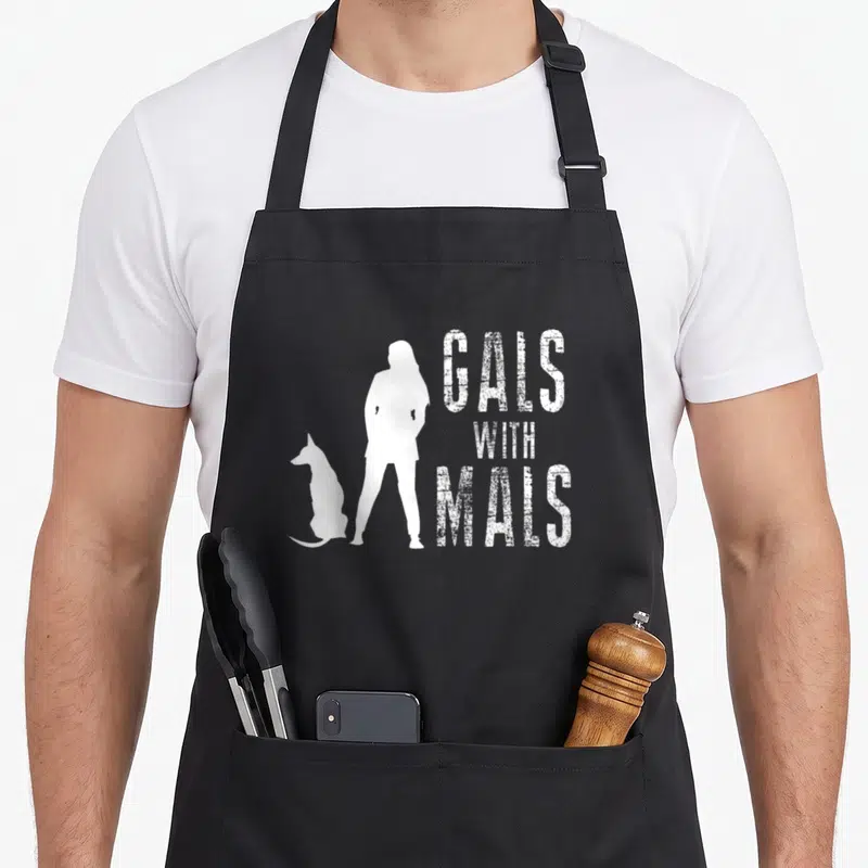 Gal malibu apron - White distressed GALS WITH MALS text beside standing woman and sitting dog silhouettes — shown on a black cotton canvas apron against a white background