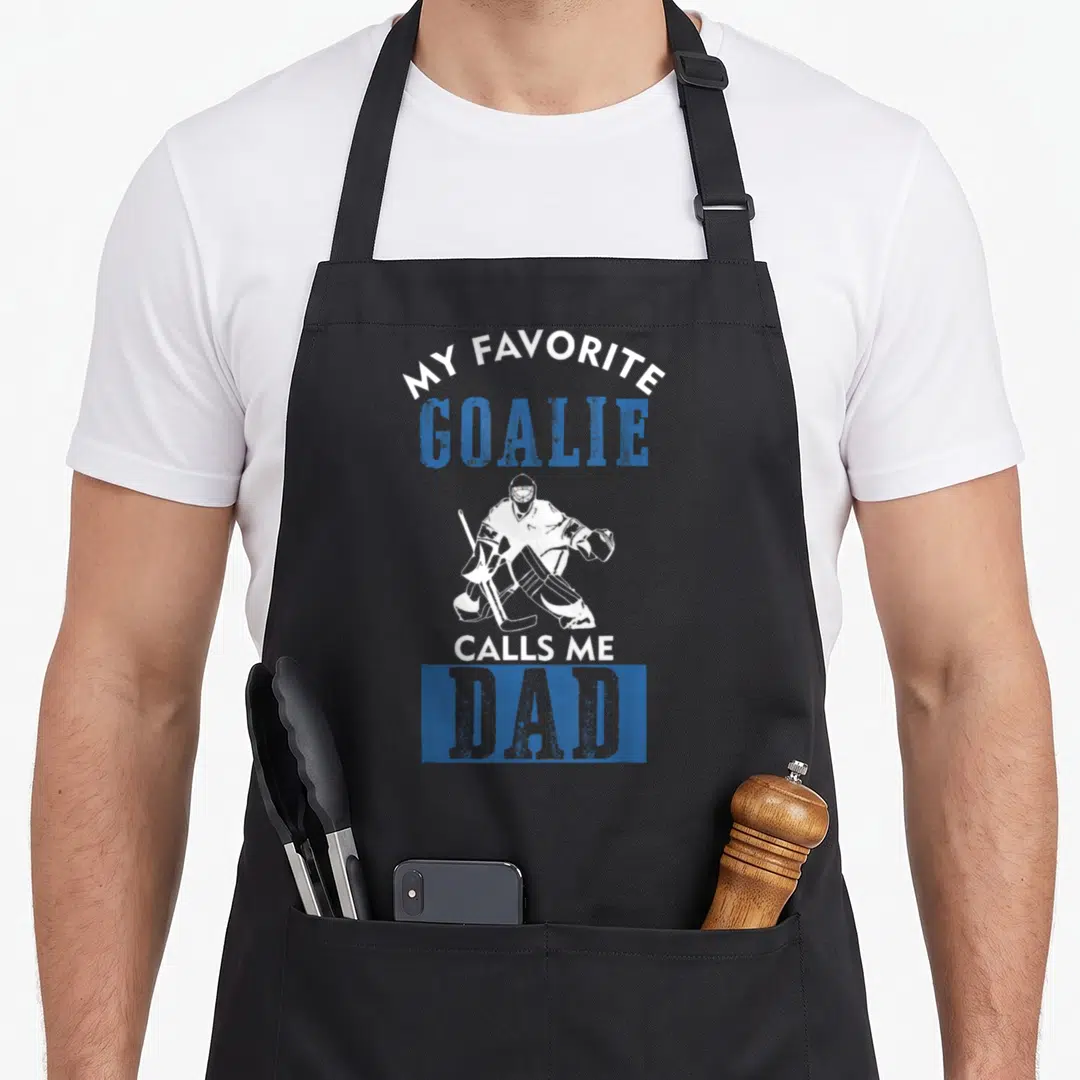 Call hockey dad apron - White goalie silhouette and text My Favorite Goalie Calls Me Dad in blue and grey distressed — shown on a black cotton canvas apron against a white background