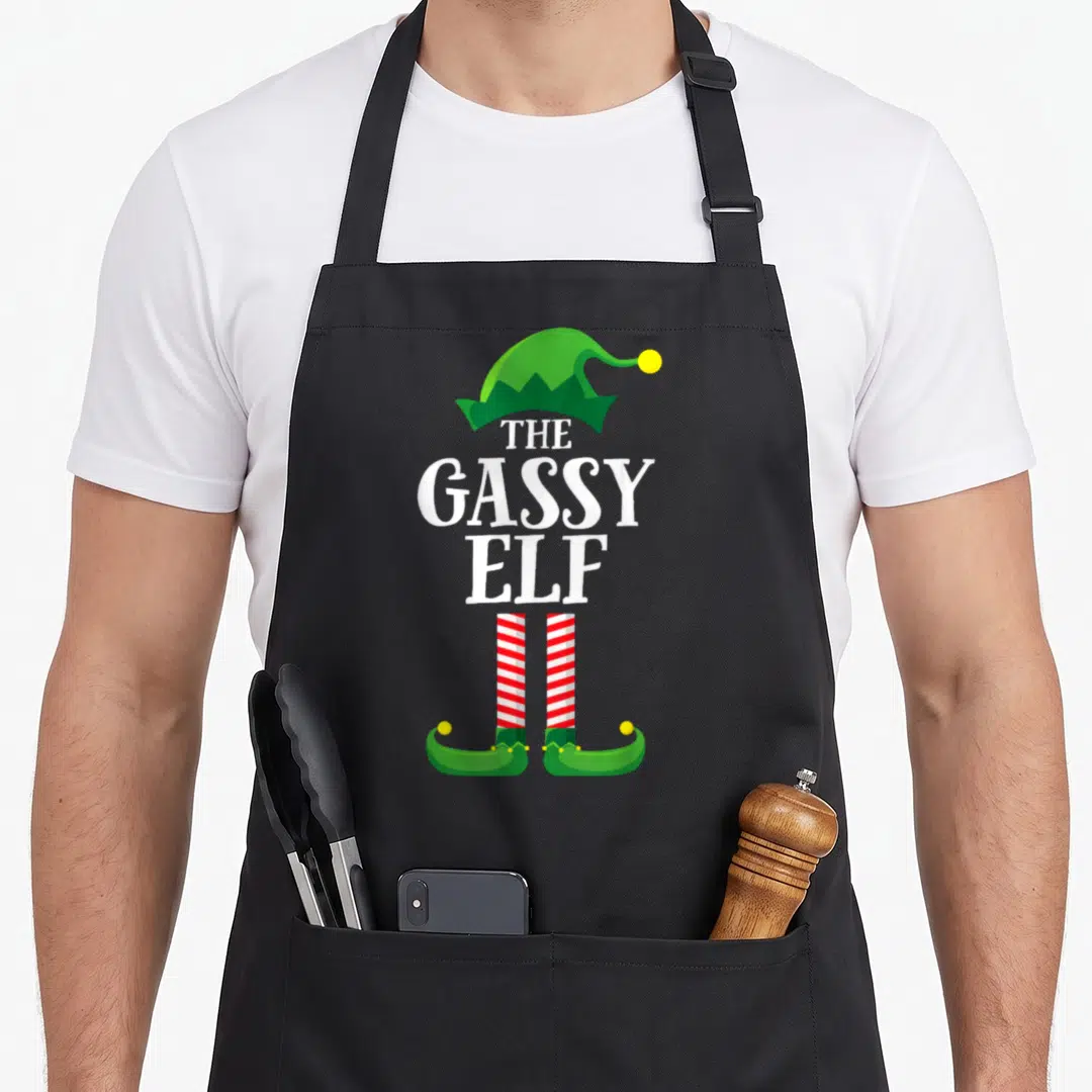 Gassy personalized family aprons - Cartoon elf hat, THE GASSY ELF text, red white striped legs, curled green shoes — shown on a black cotton canvas apron against a white background