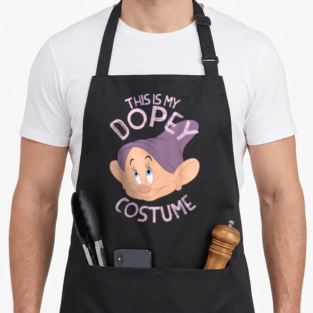 Halloween snow white apron - Dopey cartoon head with purple hat and peach skin, arched text reading THIS IS MY DOPEY — shown on a black cotton canvas apron against a white background