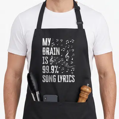 Brain karaoke apron - Distressed white text reading MY BRAIN IS 99.9% SONG LYRICS next to scattered musical notes — shown on a black cotton canvas apron against a white background