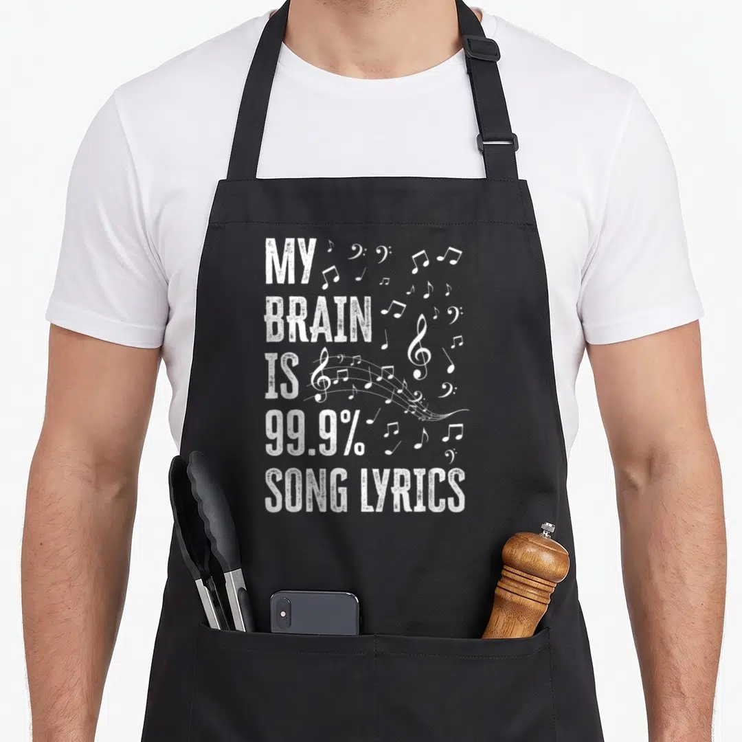 Brain karaoke apron - Distressed white text reading MY BRAIN IS 99.9% SONG LYRICS next to scattered musical notes — shown on a black cotton canvas apron against a white background