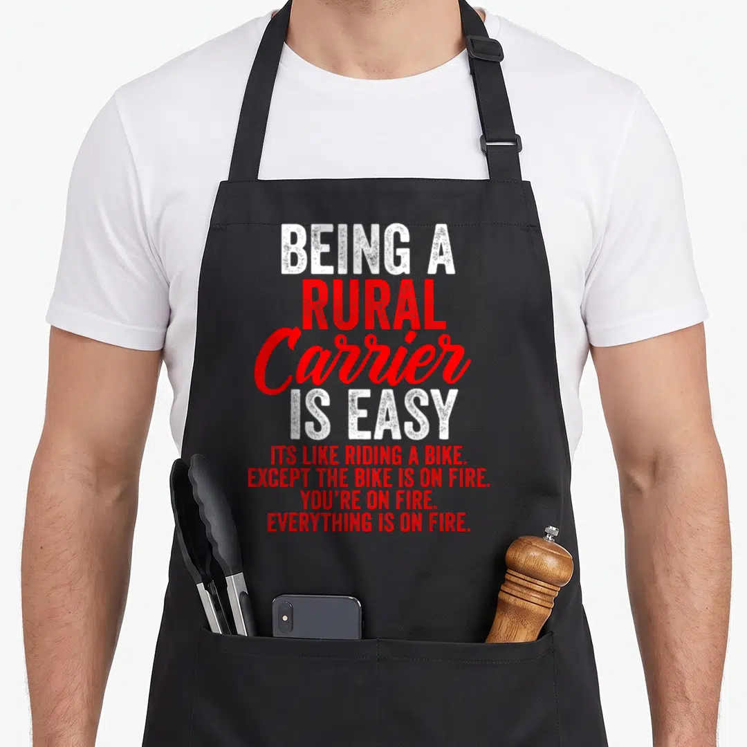Rural letter carrier apron - White and red stacked text reading BEING A RURAL Carrier IS EASY except the bike is on fire — shown on a black cotton canvas apron against a white background