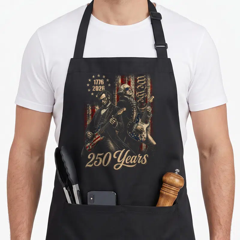 Washington playing guitar apron - Two founding fathers playing electric guitars with 1776 2026 and 250 Years text — shown on a black cotton canvas apron against a white background