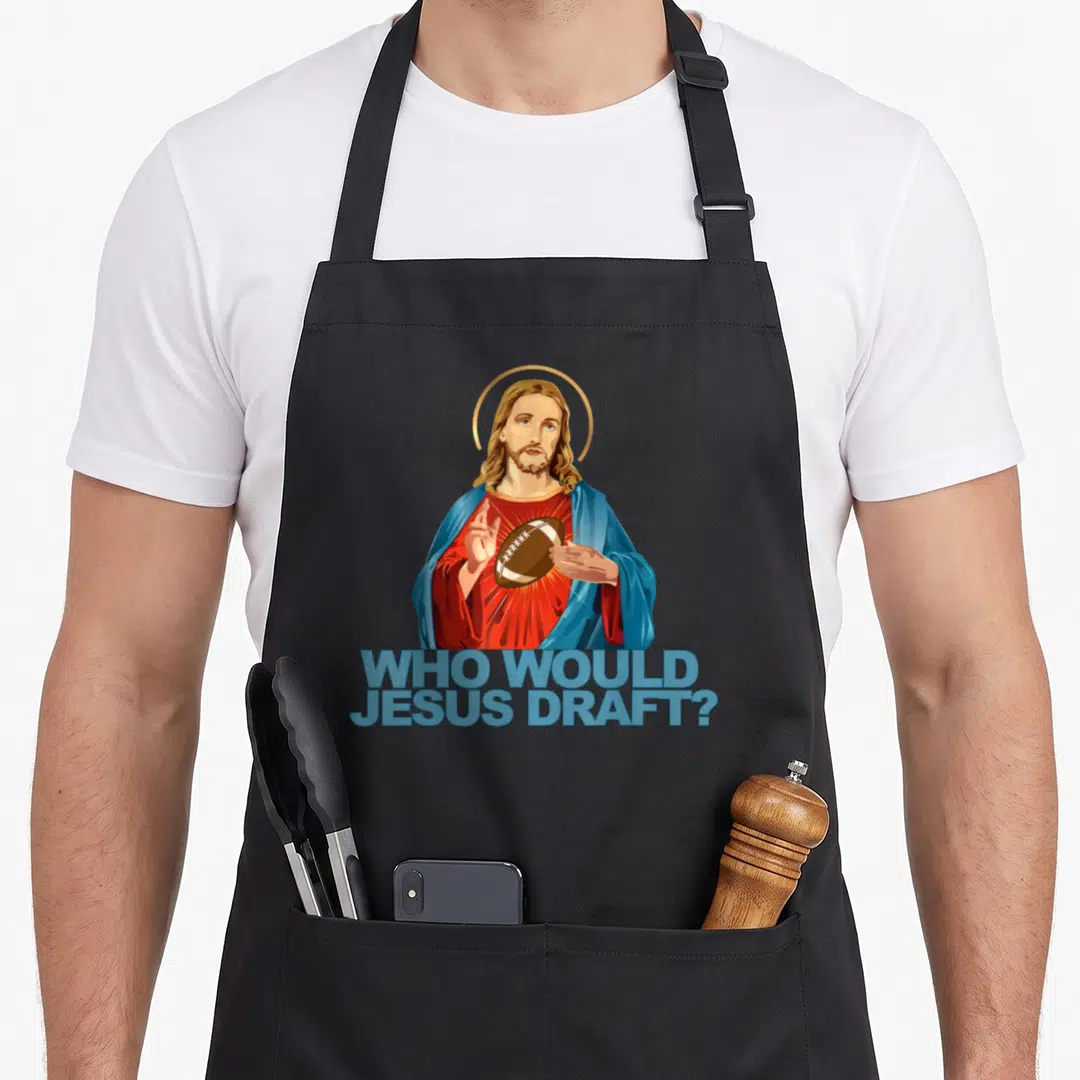 Would football apron - Cartoon Jesus holding brown football with blue text WHO WOULD JESUS DRAFT below — shown on a black cotton canvas apron against a white background