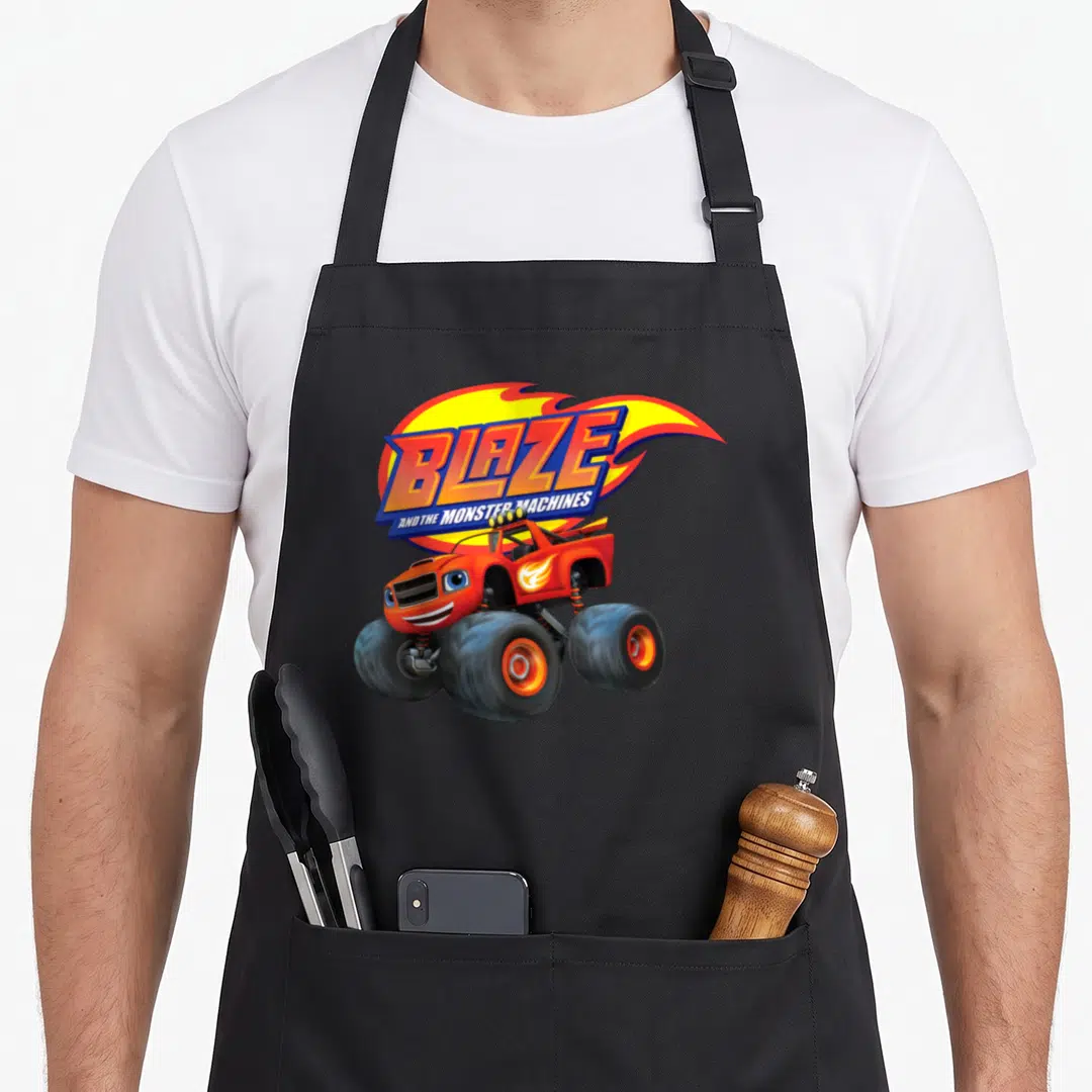 Monster machine apron - Red monster truck with blue eyes under Blaze logo and yellow flame graphic — shown on a black cotton canvas apron against a white background