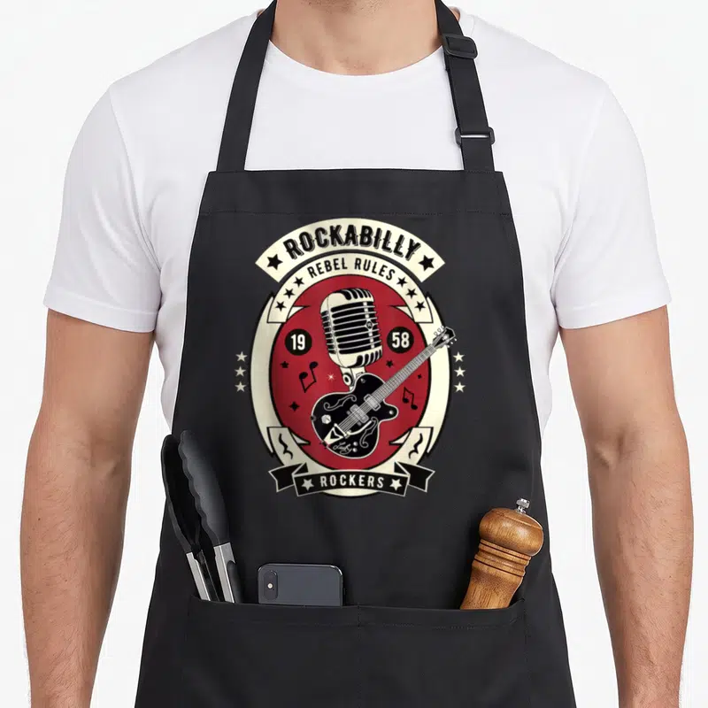 Rocker rockabilly apron - Vintage 1958 emblem with microphone, guitar, and Rebel Rules text in red and cream — shown on a black cotton canvas apron against a white background