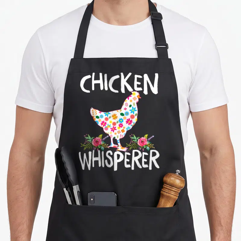 Whisperer farmer chicken apron - Floral chicken silhouette with CHICKEN WHISPERER text in watercolor style — shown on a black cotton canvas apron against a white background