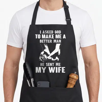 Asked wife apron - White distressed text and two hands holding, three lines above, two below, on black bib apron — shown on a black cotton canvas apron against a white background