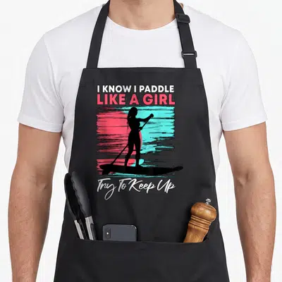 Paddle stand boarding apron - Black woman silhouette paddleboarding on pink teal background with white text I Know I — shown on a black cotton canvas apron against a white background