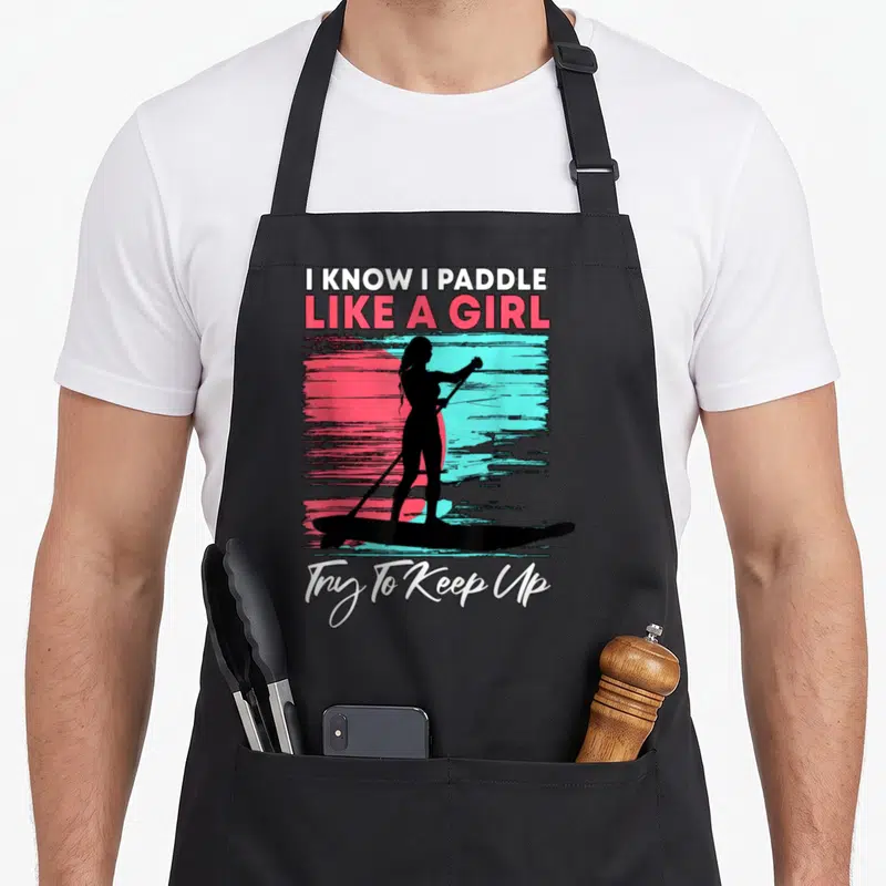 Paddle stand boarding apron - Black woman silhouette paddleboarding on pink teal background with white text I Know I — shown on a black cotton canvas apron against a white background