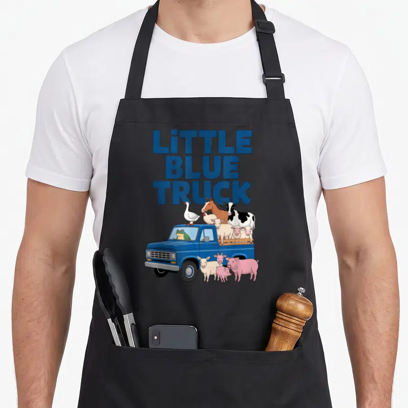 Blue truck apron - Stacked LITTLE BLUE TRUCK text above cartoon truck with frog driver and assorted farm animals — shown on a black cotton canvas apron against a white background