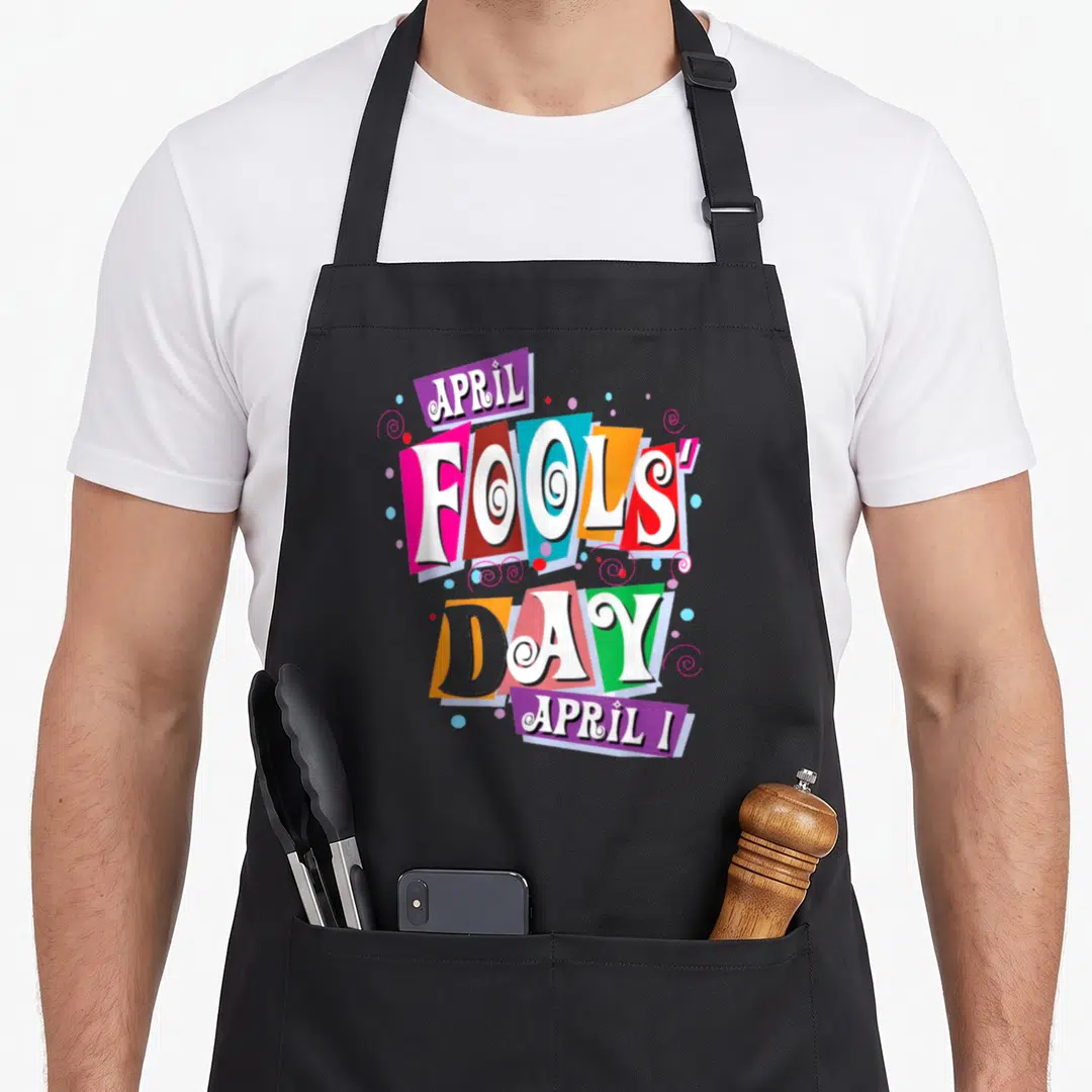 Fool prank apron - April Fools Day text on tilted colorful rectangles with spirals — shown on a black cotton canvas apron against a white background