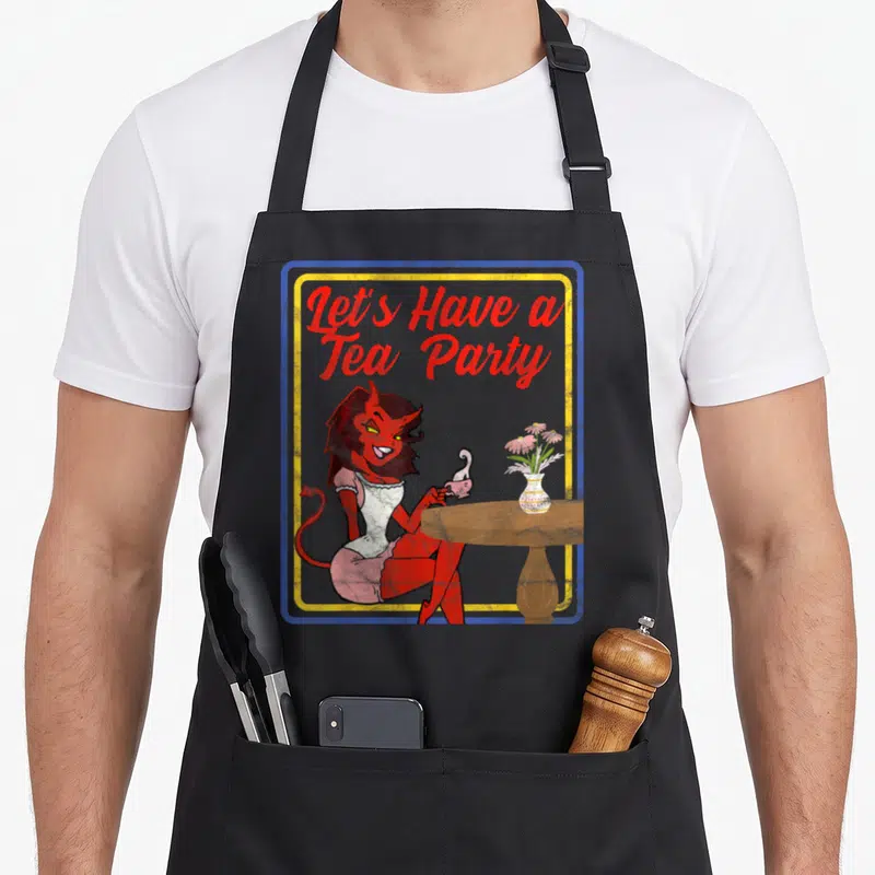 Horror tea party aprons - Red devil woman seated at table with teacup and flowers under Let's Have a Tea Party text — shown on a black cotton canvas apron against a white background