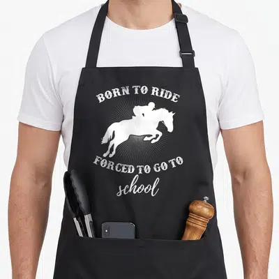 School horse apron - White distressed horse and rider silhouette with arched text over sunburst rays — shown on a black cotton canvas apron against a white background