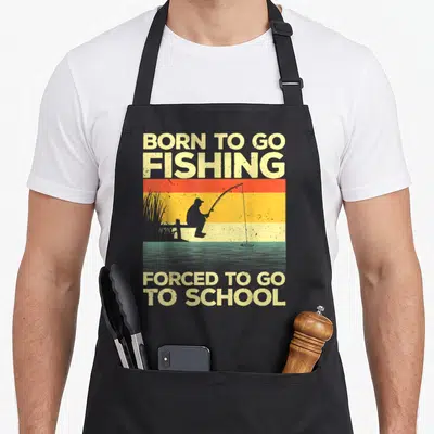 Fisherman fish fishing aprons - Born to go fishing forced to go to school text with fisherman silhouette on striped — shown on a black cotton canvas apron against a white background