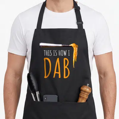 Dab hash lover apron - Silver tool with orange oil drip and THIS IS HOW I DAB text — shown on a black cotton canvas apron against a white background