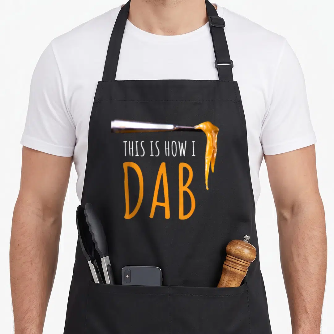 Dab hash lover apron - Silver tool with orange oil drip and THIS IS HOW I DAB text — shown on a black cotton canvas apron against a white background