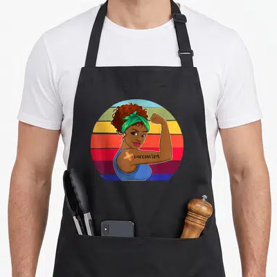 Vaccinated african american aprons - Cartoon woman flexing arm with vaccinated text and bandage on striped circle — shown on a black cotton canvas apron against a white background