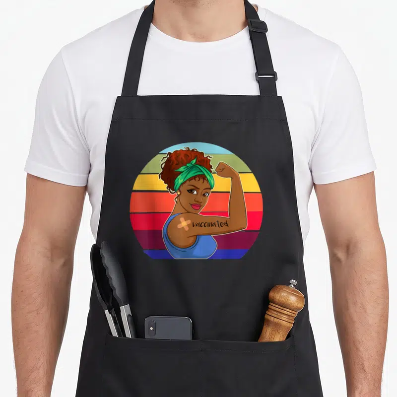 Vaccinated african american aprons - Cartoon woman flexing arm with vaccinated text and bandage on striped circle — shown on a black cotton canvas apron against a white background