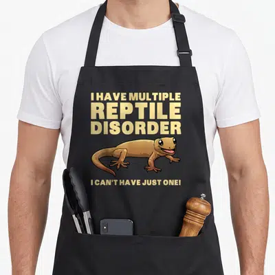 Crested dragon apron - Cartoon lizard with text I HAVE MULTIPLE REPTILE DISORDER I CAN'T HAVE JUST ONE — shown on a black cotton canvas apron against a white background