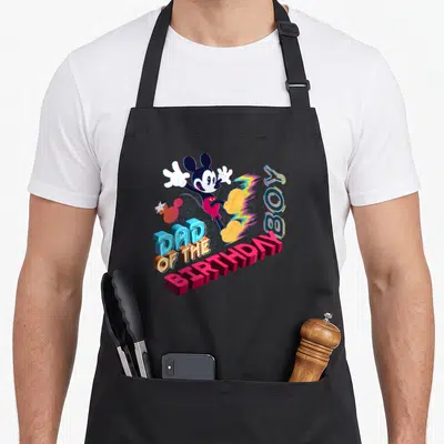Cute star family aprons - Jumping Mickey Mouse above 3D text DAD OF THE BIRTHDAY BOY in blue pink yellow red — shown on a black cotton canvas apron against a white background