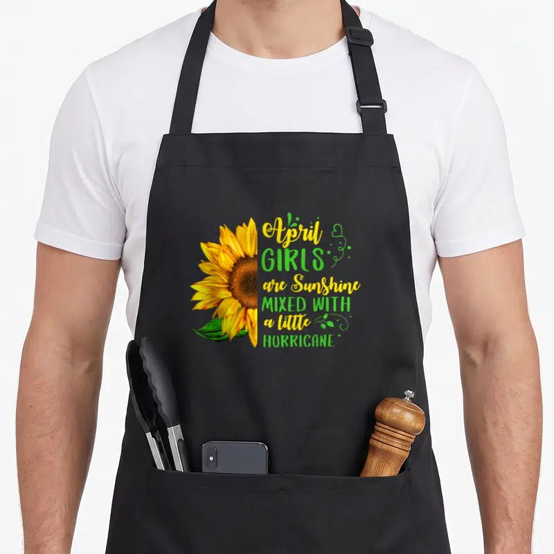 Hurricane birthday apron - Sunflower and April girls are sunshine mixed with hurricane text design — shown on a black cotton canvas apron against a white background