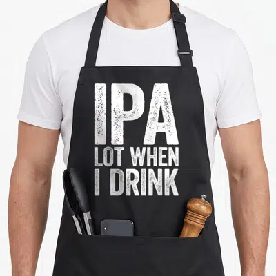Funny ipa beer apron - White distressed stacked text reading IPA LOT WHEN I DRINK — shown on a black cotton canvas apron against a white background