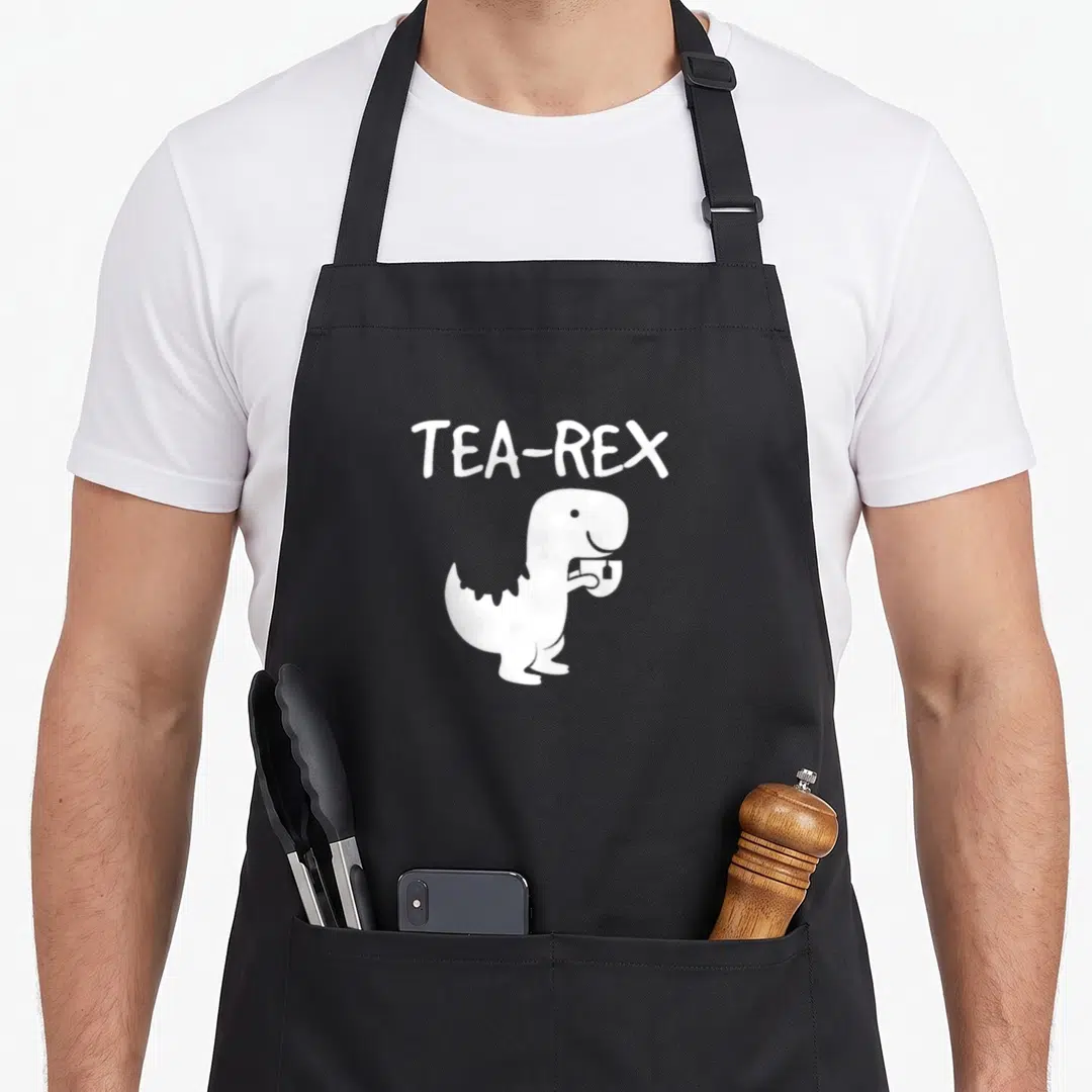 Tyrannosaurus tea party aprons - White TEA-REX text above cartoon dinosaur holding teacup — shown on a black cotton canvas apron against a white background