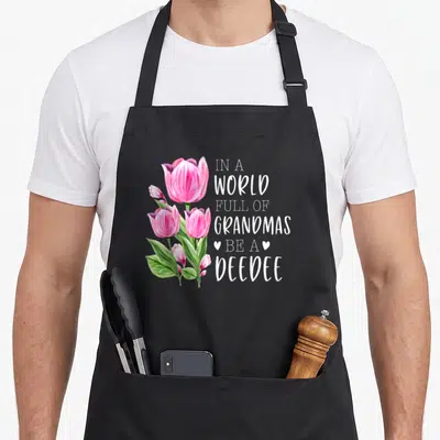 Grandmas tulip apron - Pink watercolor tulips next to In A World Full Of Grandmas Be A DeeDee text — shown on a black cotton canvas apron against a white background